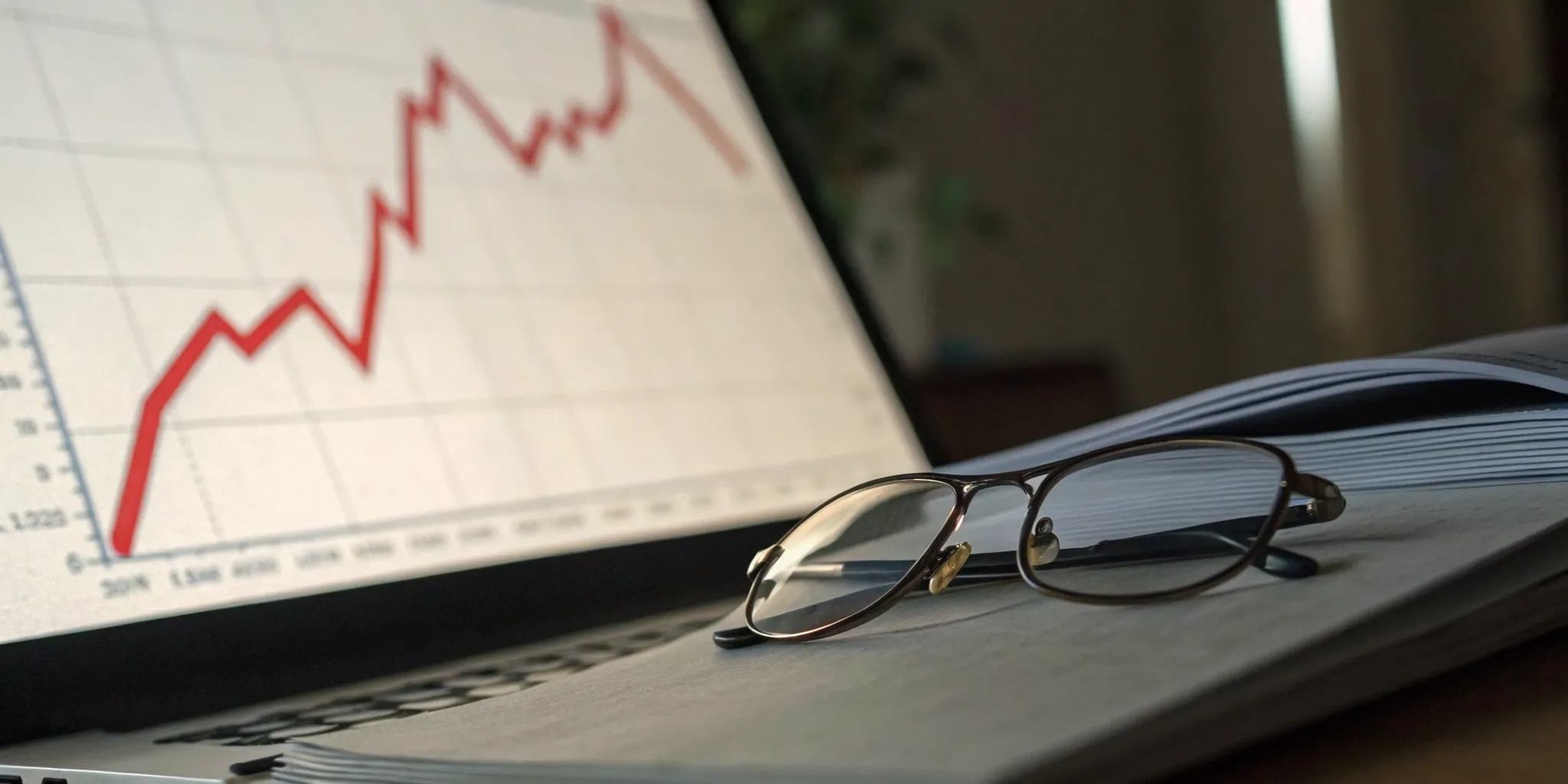 Financial graph on laptop with glasses and open book.